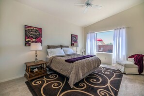 A bedroom with a bed, bedside tables, a ceiling fan, a window with curtains, and artwork on the walls.