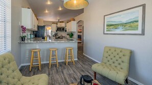 Una cucina moderna con isola centrale, sgabelli da bar e zona pranzo con una sedia imbottita verde.