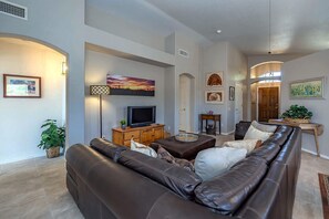 Ein Wohnzimmer mit einem braunen Ledersofa, einem Fernseher und einem Gemälde an der Wand.