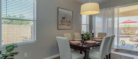 A dining area with a table set for four, a hanging light fixture, and a large window with blinds.