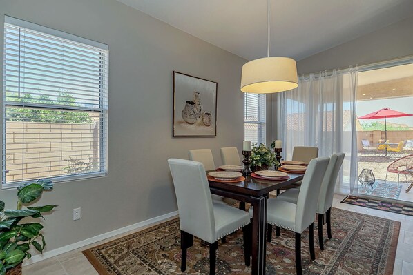 A dining area with a table set for four, a hanging light fixture, and a large window with blinds.