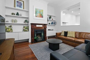 Un soggiorno moderno con camino, divano in pelle e tavolino in legno. Si notano scaffali con oggetti decorativi e un grande quadro.