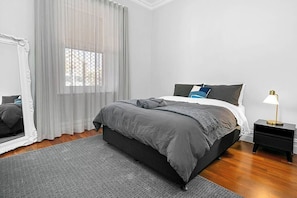 A bedroom with a bed, a nightstand, a lamp, a mirror, and sheer curtains.