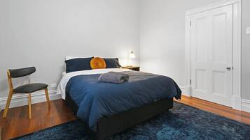 A bedroom with a bed, a chair, a nightstand, a lamp, and a door.