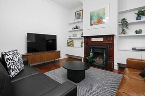 A modern living room with a flat-screen TV, a fireplace, a sofa, and a coffee table. - Luxury Stay 5 Mins From CBD - 3Bdrm, 2Bthrm (Thebarton)