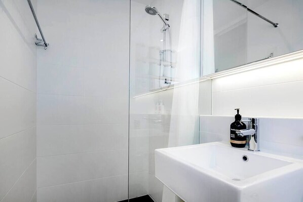 A modern bathroom with a glass shower enclosure, a white sink with a soap dispenser, and a mirror above the sink.