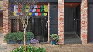 A modern building with a brick facade, a black metal gate, and a small tree in the entrance. - Serenity in the City - 1BD Studio, Wifi, CBD (Adelaide)