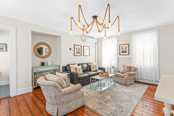 A modern living room with a black leather sofa, two armchairs, a glass coffee table, and a unique rope chandelier.