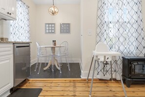 A kitchen with a dining table, chairs, a white high chair, a stove, and a hanging light fixture. - Historic 6-Bed Pet-Friendly Home, Walk to Seaport (Stonington)