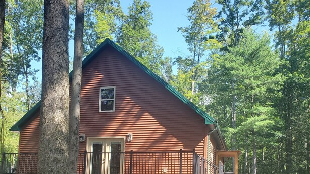 A rustic cabin with a red exterior, surrounded by a natural landscape with trees and rocks.