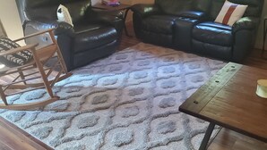 A living room with two black leather sofas, a wooden rocking chair, a patterned rug, and a wooden coffee table.