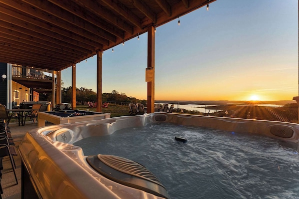 A hot tub under a wooden pergola with a sunset view.