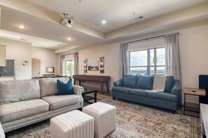 A spacious living room with a sofa, ottoman, and a piano.