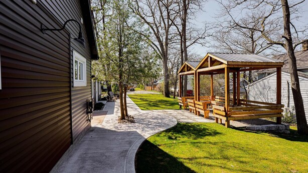 Eine Holzterrasse mit Bänken, einer überdachten Sitzgelegenheit und einem Haus mit geneigtem Dach.