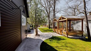 Una terraza de madera con bancos, una zona de estar cubierta y una casa con techo inclinado.
