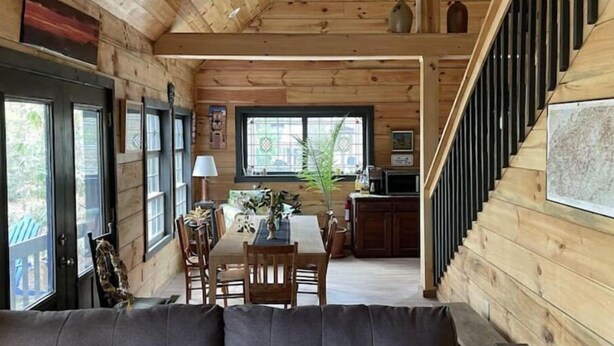 A wooden cabin interior with a dining area, kitchen, and staircase. - The Pottery Cabin (Leicester)