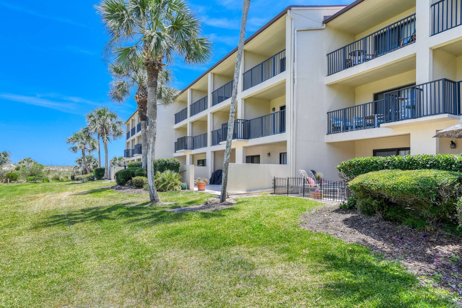 A multi-story hotel with balconies, a well-maintained lawn, and palm trees.