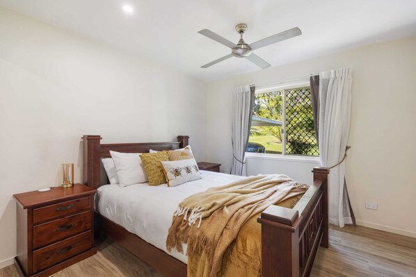 A bedroom with a wooden bed, a nightstand, a ceiling fan, and a window with curtains.