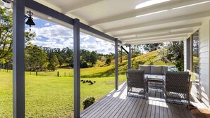 A covered outdoor area with a wooden deck, wicker furniture, and a view of a grassy landscape. - Bellemarie - An Unforgettable Farm Stay (Bellthorpe)