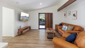 A modern living room with a wooden floor, a brown leather sofa, a wooden coffee table, and a TV mounted on the wall. - Bellemarie - An Unforgettable Farm Stay (Bellthorpe)