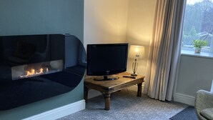 A living room with a fireplace, a television on a wooden table, and a view of the outdoors through a window with curtains. - Stay in a grand old house, close to Hebden Bridge with parking & pet friendly.   (Hebden Bridge)