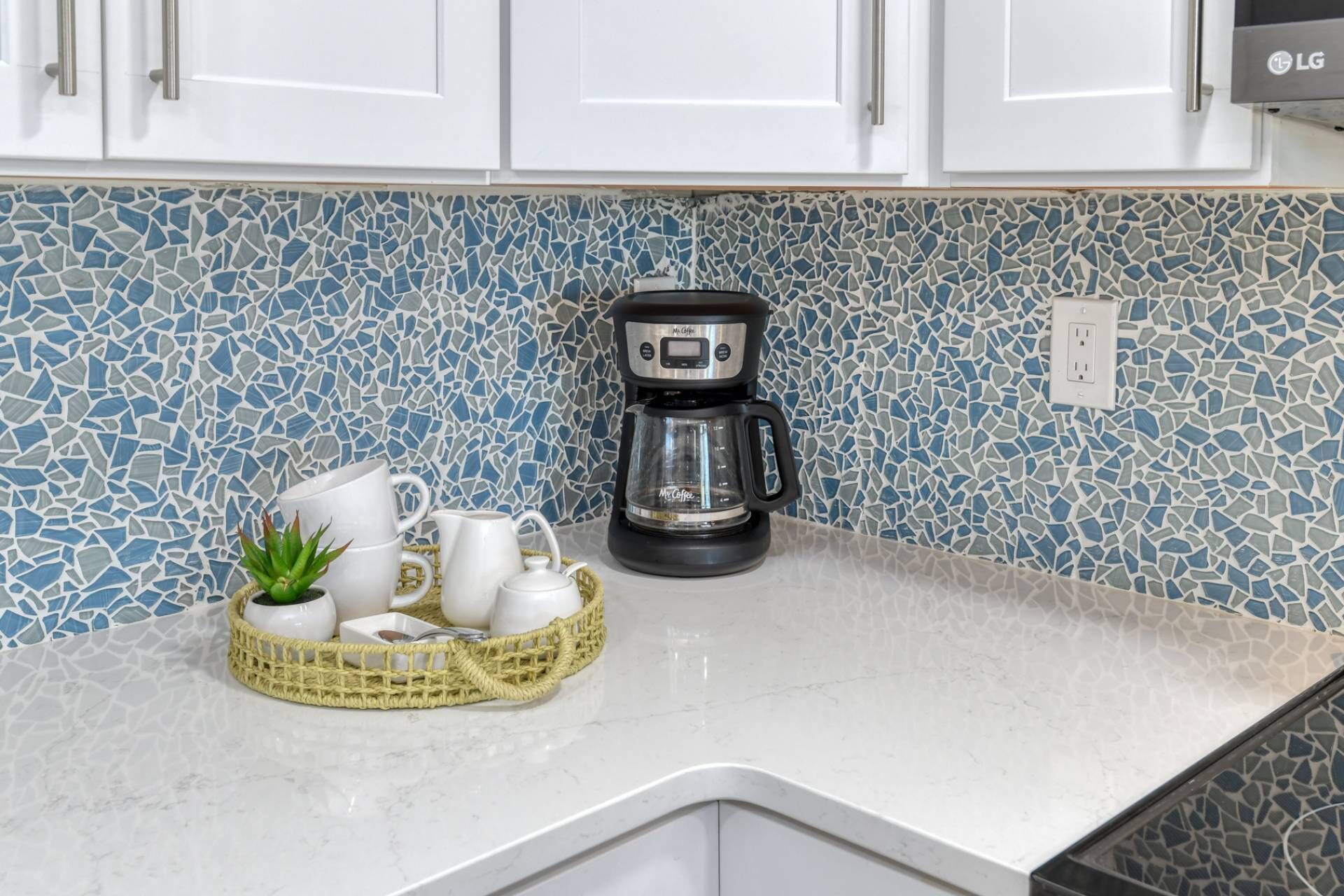 A kitchen with white cabinets, a coffee maker, and a mosaic backsplash.