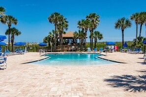 A pool area with lounge chairs and umbrellas, surrounded by palm trees.