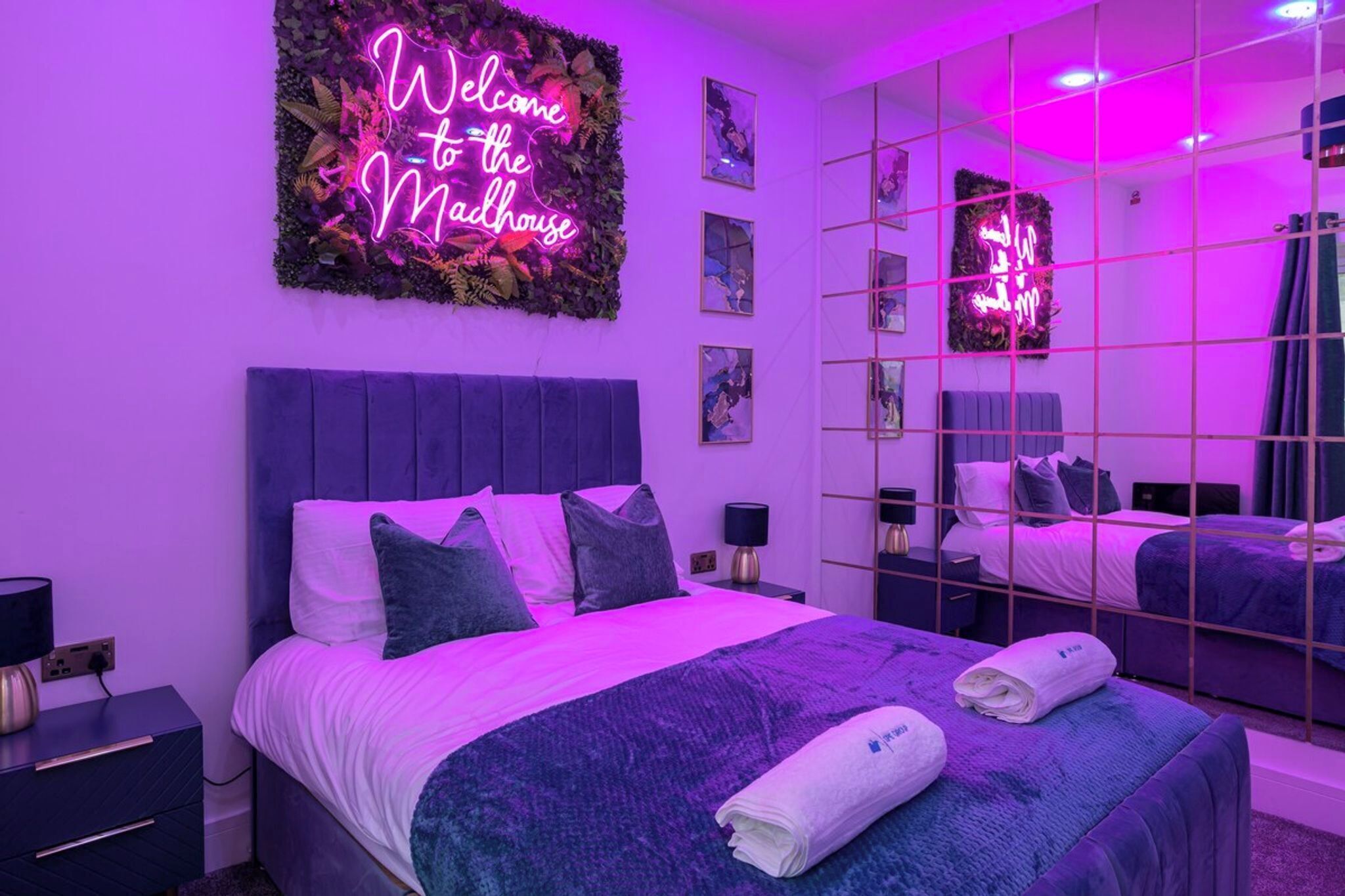 Une chambre d’hôtel moderne, avec un néon, un grand miroir et un lit parfaitement fait.