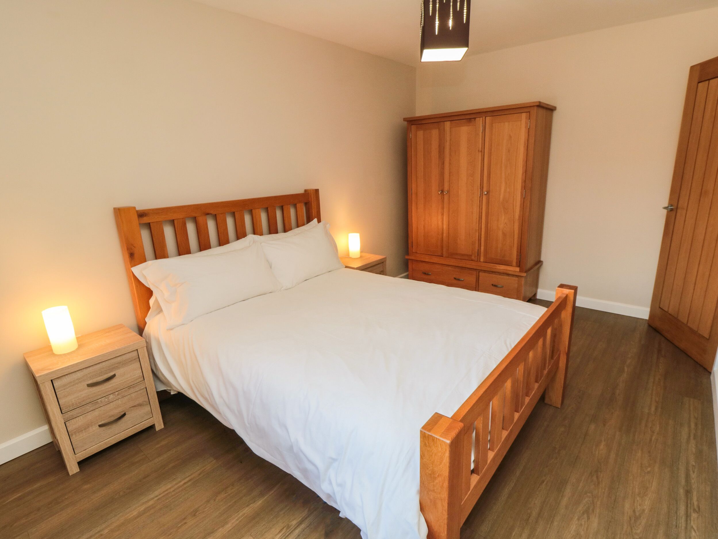 A bedroom with a wooden bed, nightstands, a wardrobe, and a ceiling light.