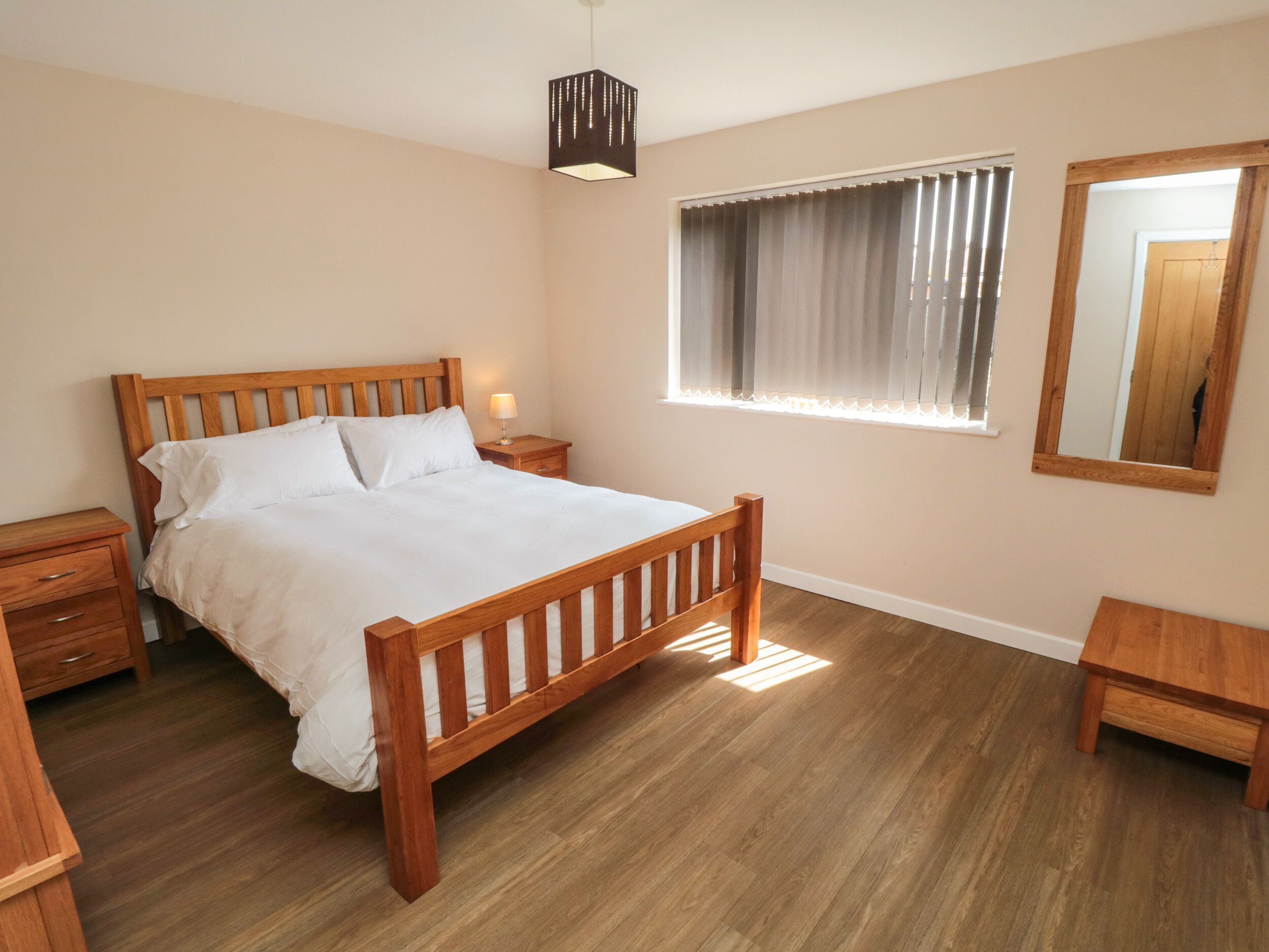 A bedroom with a wooden bed, bedside tables, a window with curtains, and a hanging light fixture.