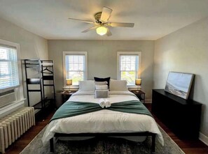 Une chambre à coucher comprenant un lit, deux tables de chevet, un ventilateur de plafond et un radiateur.