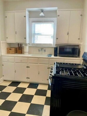 Une cuisine avec des meubles blancs, un carrelage noir et blanc, un four à micro-ondes et une cuisinière.