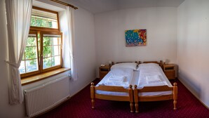 Une chambre avec un lit double, un radiateur, une fenêtre avec des rideaux, une table de chevet avec une lampe et un tableau coloré au mur.