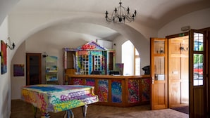 Une pièce avec un piano recouvert de graffitis colorés, un comptoir d’accueil en bois et un lustre.