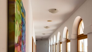 Un couloir avec un tapis rouge, des murs blancs et des œuvres d’art colorées sur le côté gauche.