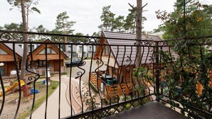 A view from a balcony with a wrought iron railing, overlooking a playground and several wooden cabins with sloped roofs.