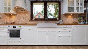 A kitchen with white cabinets, a built-in oven, a window with a view of a house, and a checkered valance above the window.