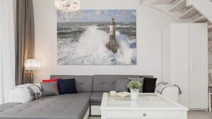 A modern living room with a grey sectional sofa, a white coffee table, and a painting of a lighthouse on the wall. - Comfortable holiday home with garden, summer pool (Pobierowo)