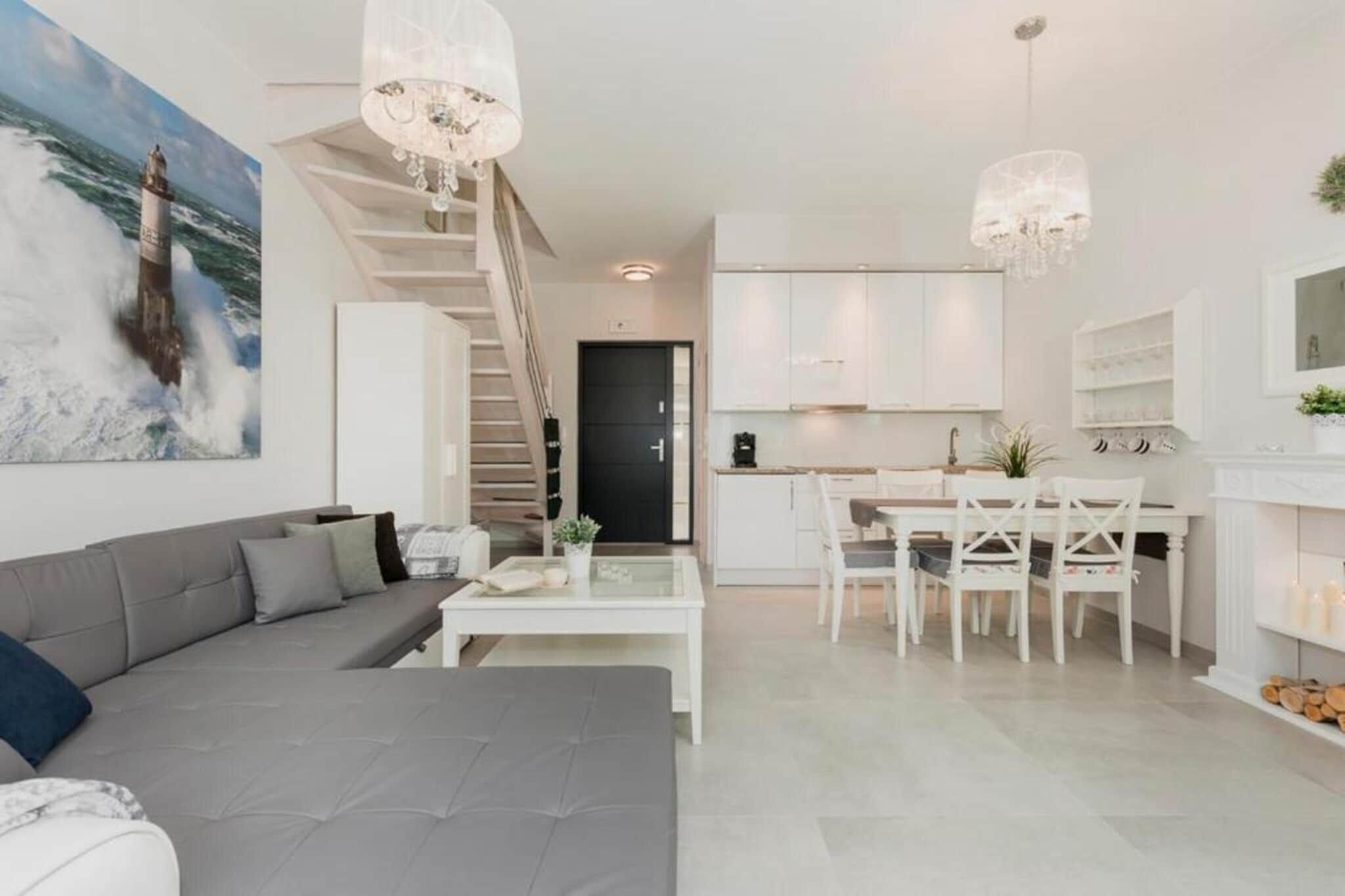 A modern living room with a grey sofa, a dining area with white chairs, and a staircase leading to another level.