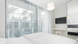 A modern hotel room with a large bed, a desk with a chair, a flat-screen TV, and a large window with sheer curtains. - Comfortable holiday home with garden, summer pool (Pobierowo)