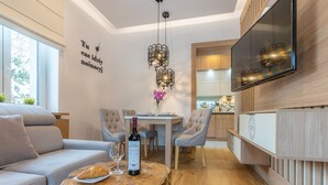 Una sala moderna con un sofá, una mesa de centro redonda de madera, una mesa de comedor con sillas, un televisor montado en la pared y un adorno mural.