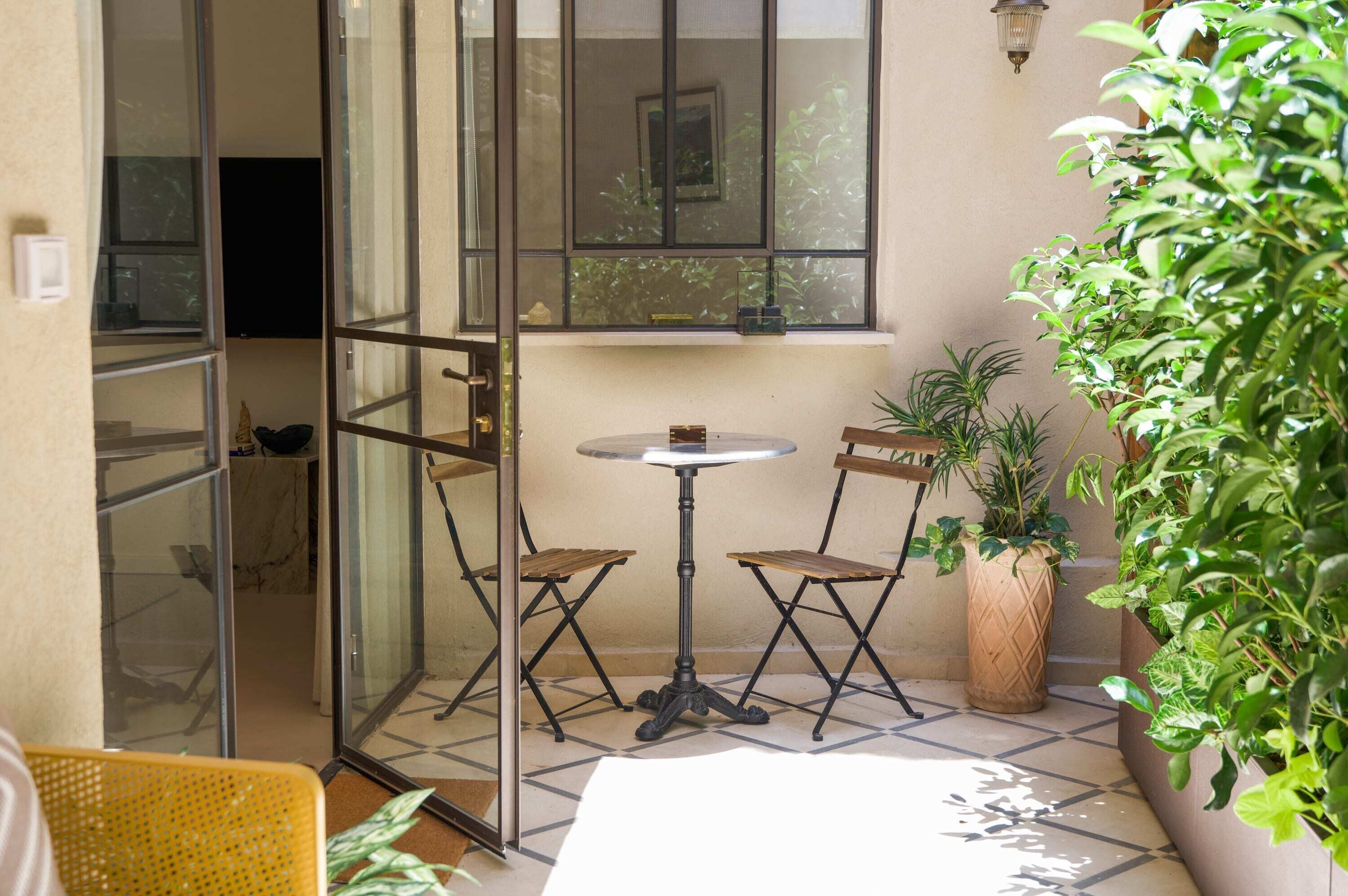A glass door leading to a patio area with a round table and two chairs, a potted plant, and a yellow chair.
