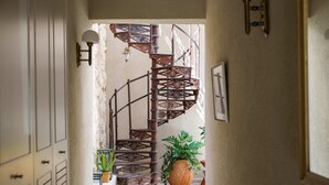A spiral staircase with intricate woodwork, a potted plant, and a wall-mounted light fixture in a hallway. - Luxurious Urban Retreat with Private Outdoor Area (Tel Aviv-Yafo)