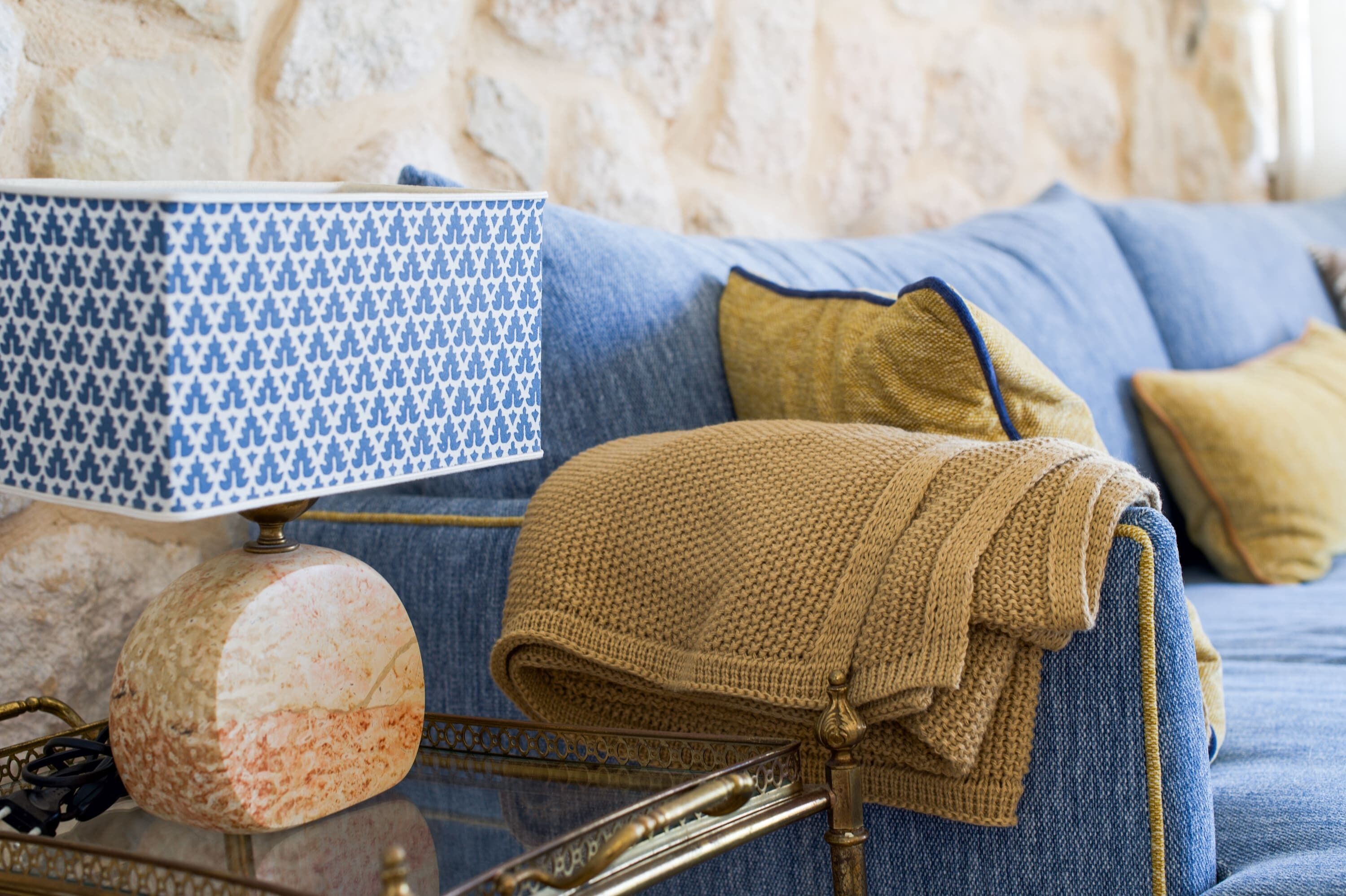 Une pièce chaleureuse avec une lampe à motifs, un plaid en tricot et un canapé bleu, le tout adossé à un mur en pierre.