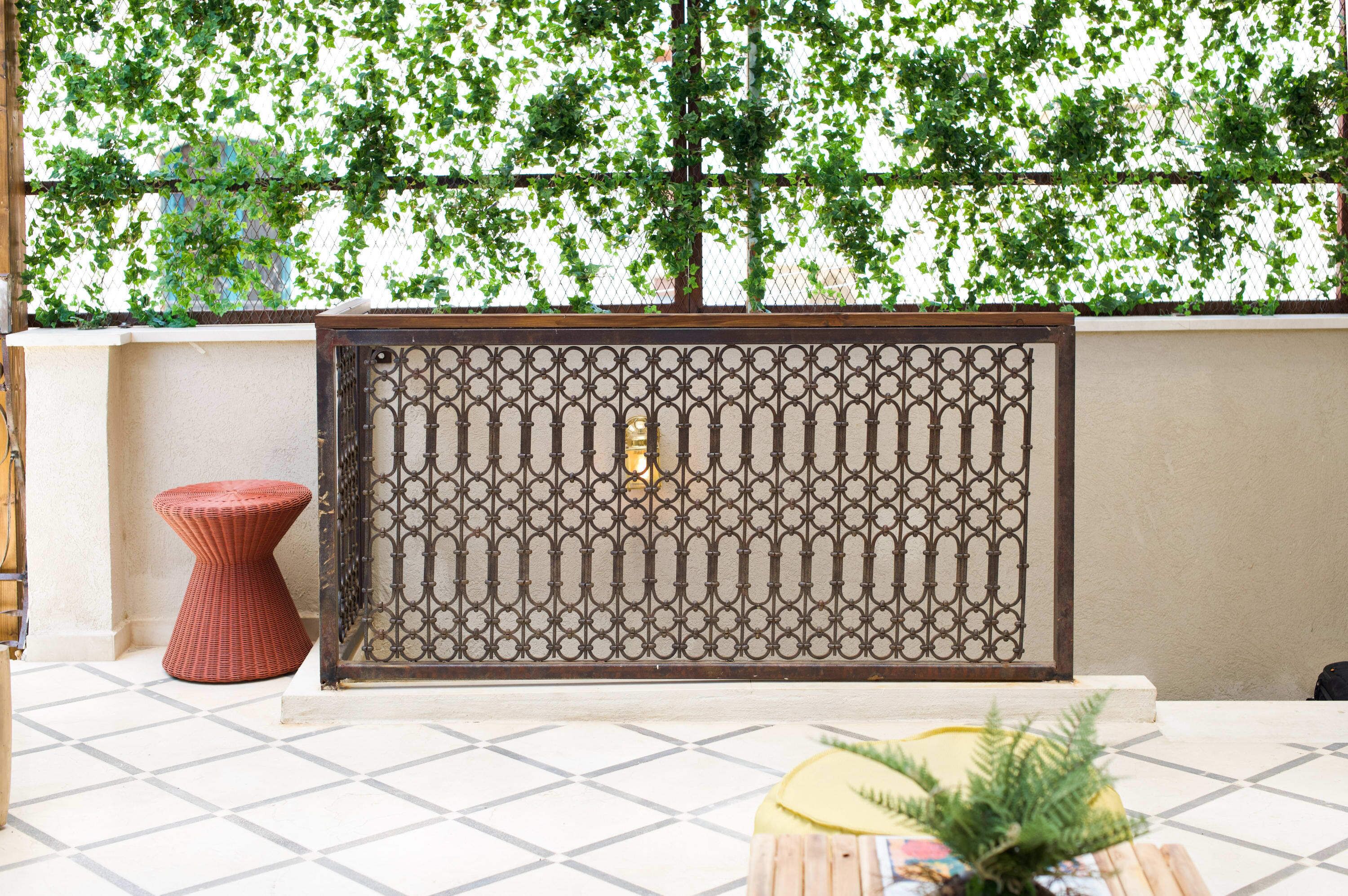 A room with a patterned metal partition, a red stool, and a potted plant on a tiled floor.