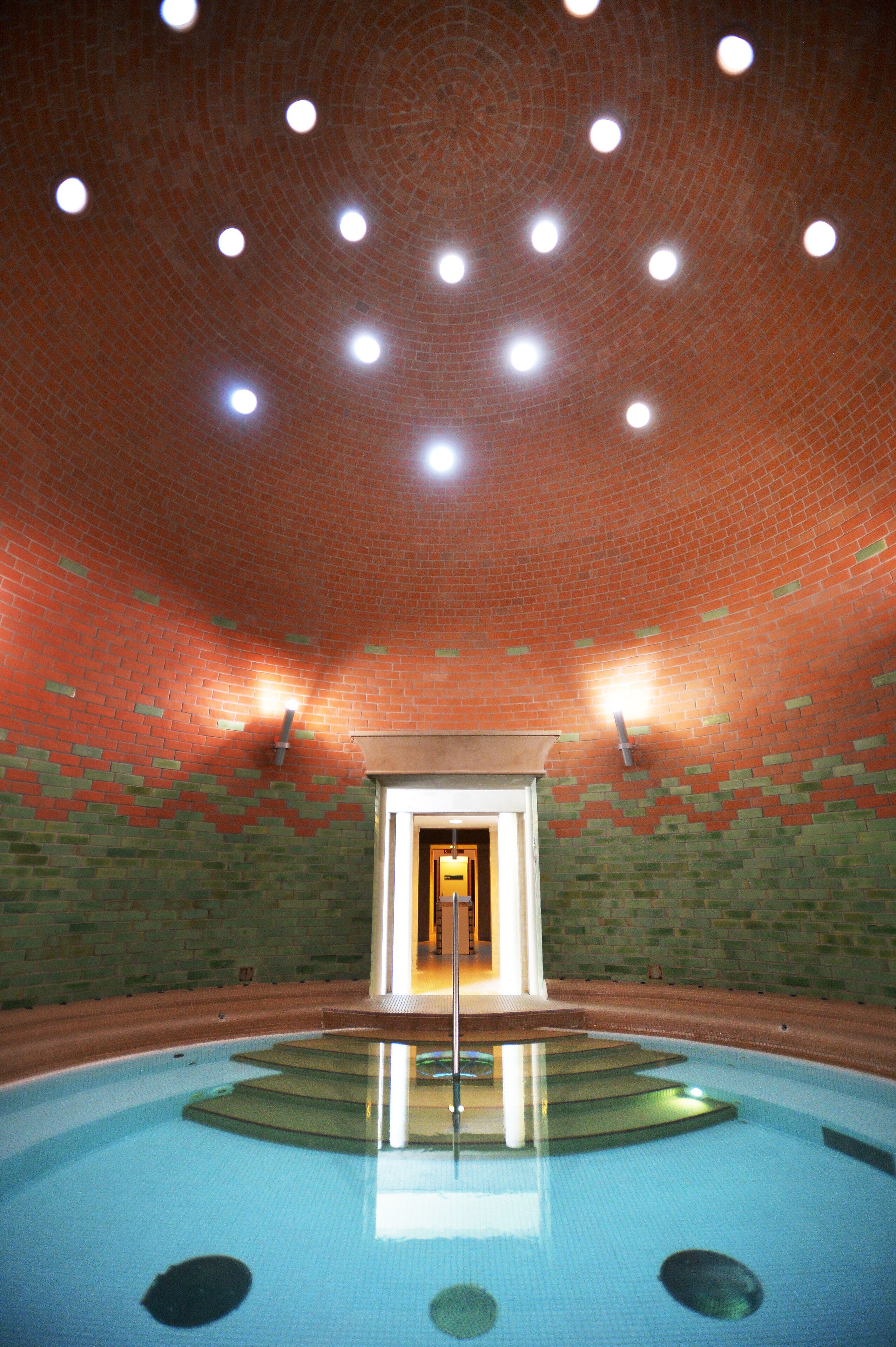 An indoor swimming pool with a brick ceiling and a central light fixture.