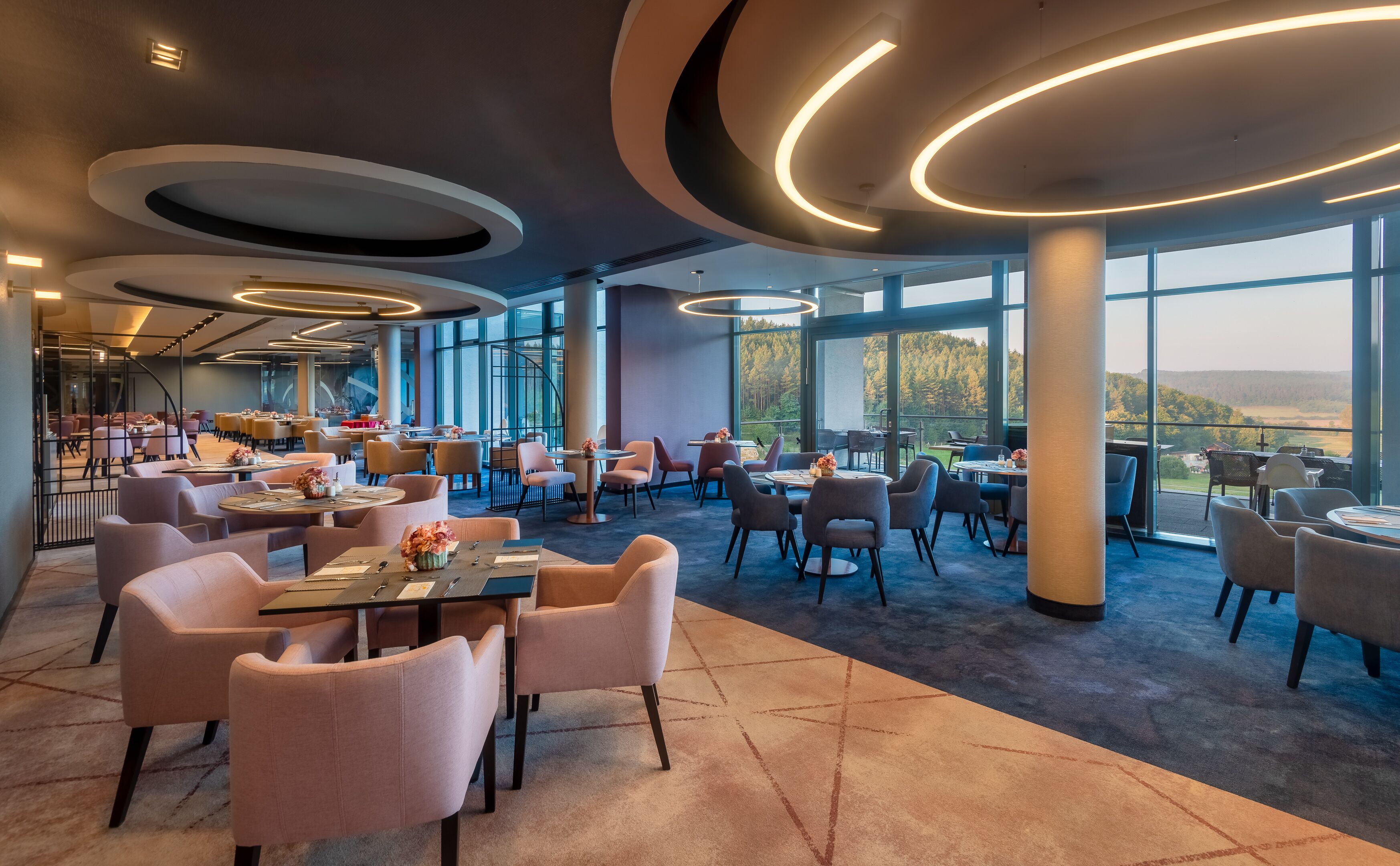 Restaurante moderno com vista panorâmica, com mesas e cadeiras redondas e um espaço amplo com grandes janelas.