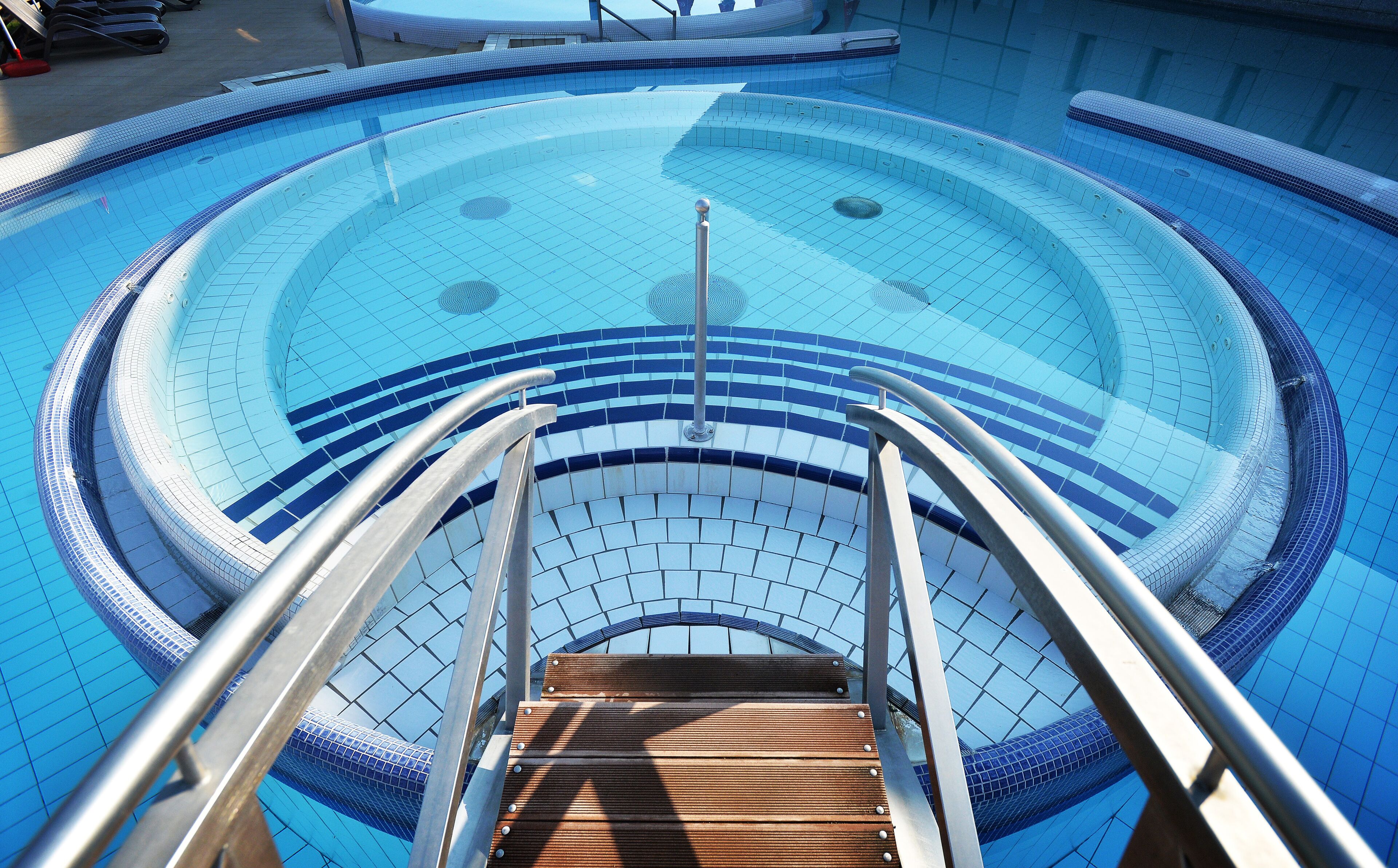 Una piscina circular con una fuente central, rodeada por un suelo de baldosas y barandillas de metal.