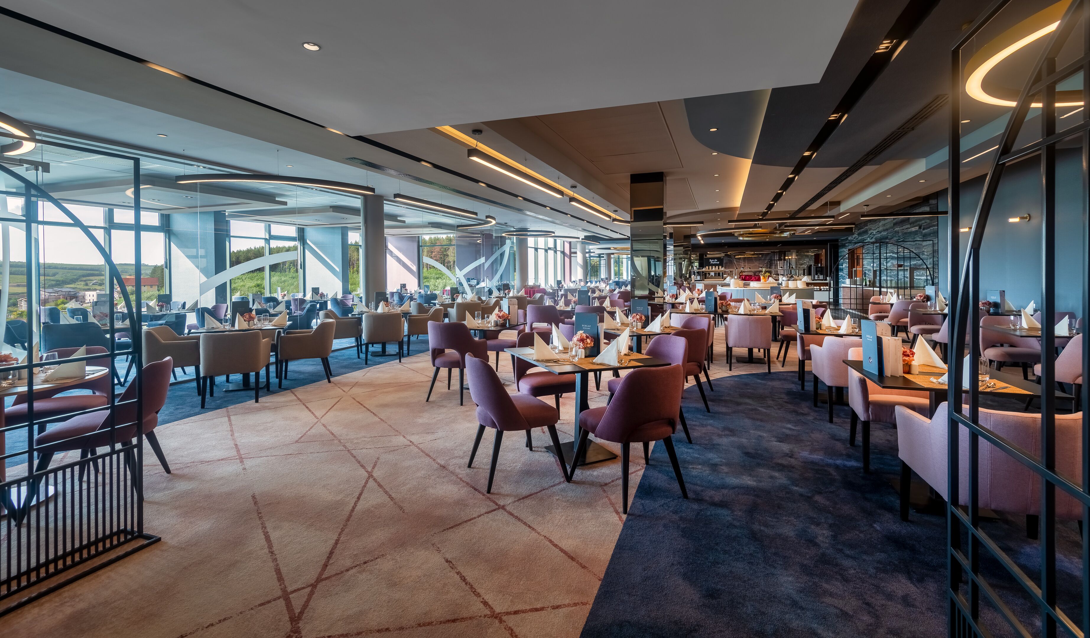 Een modern restaurant met een panoramisch uitzicht, met een mix van ronde en rechthoekige tafels en diverse zitmogelijkheden.