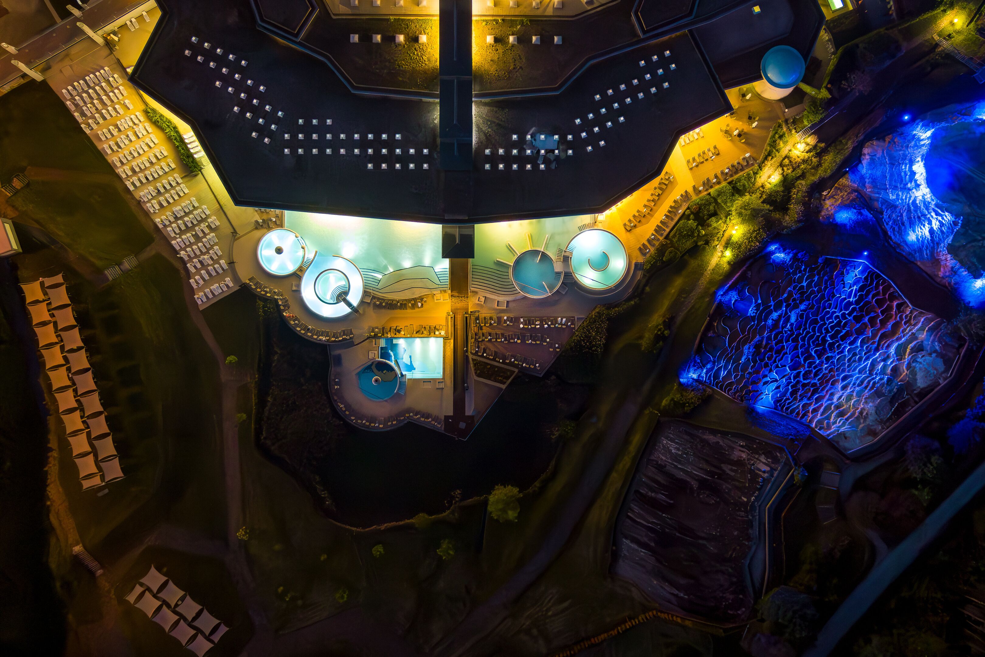 An aerial view of a hotel with multiple dining areas, a central pool, and a surrounding garden.